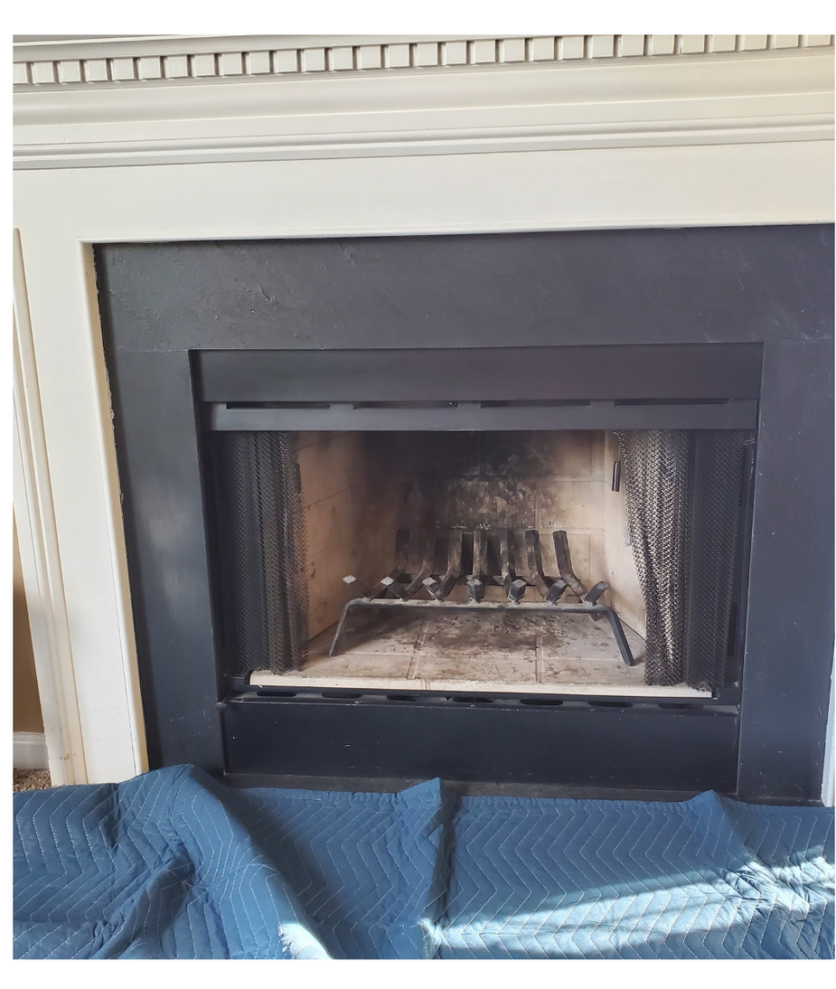 Black fireplace insert with brass log holder, set in a white mantel and covered by a blue blanket.