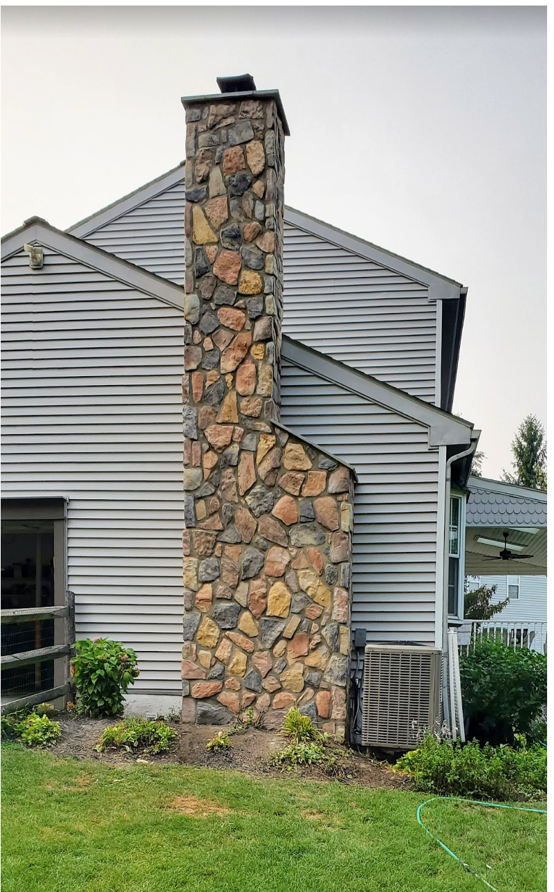 Stone chimney on the side of a gray house with a green lawn in front