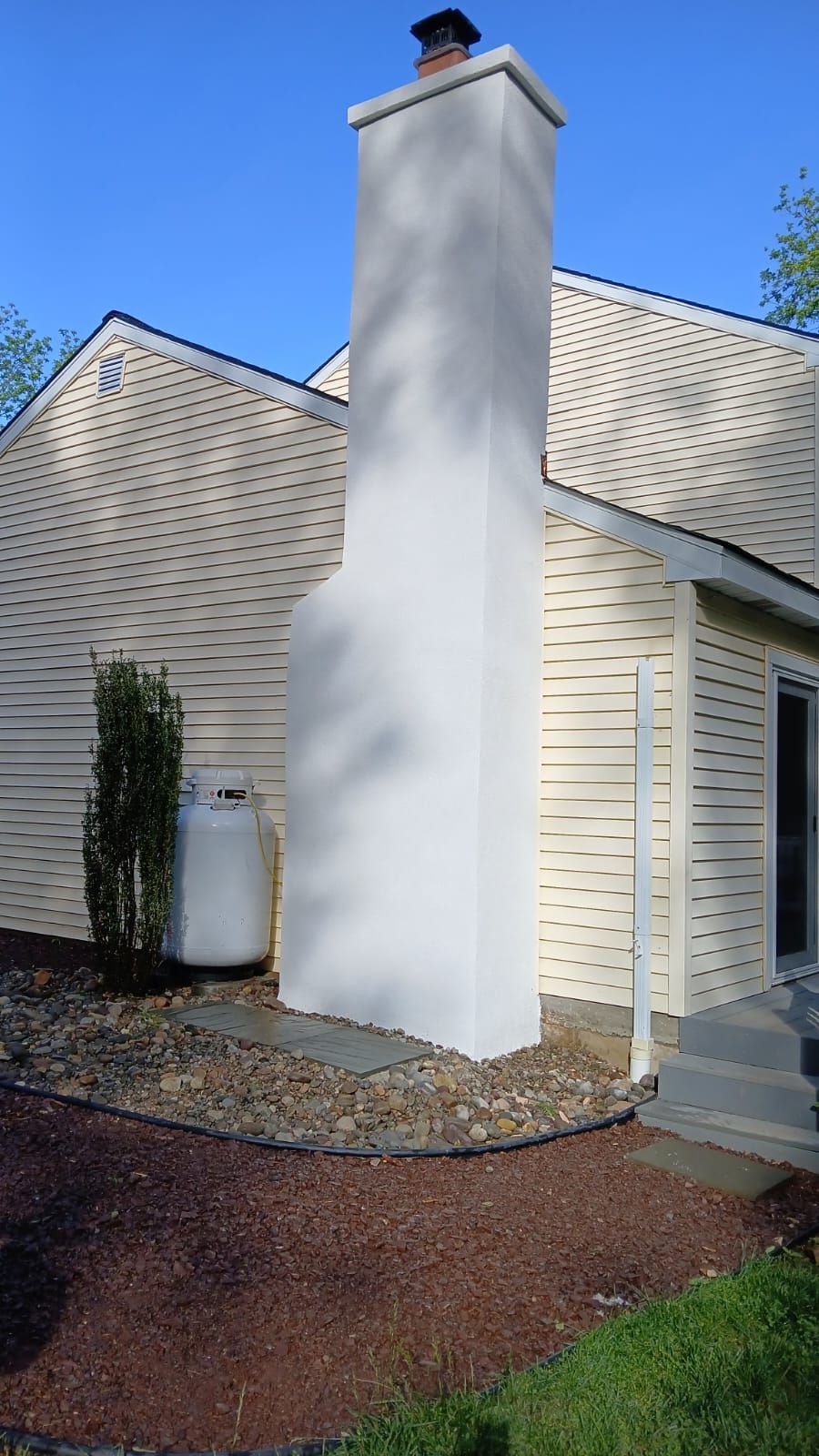 A person uses a trowel to apply mortar between bricks on a chimney structure on a red-tiled roof.