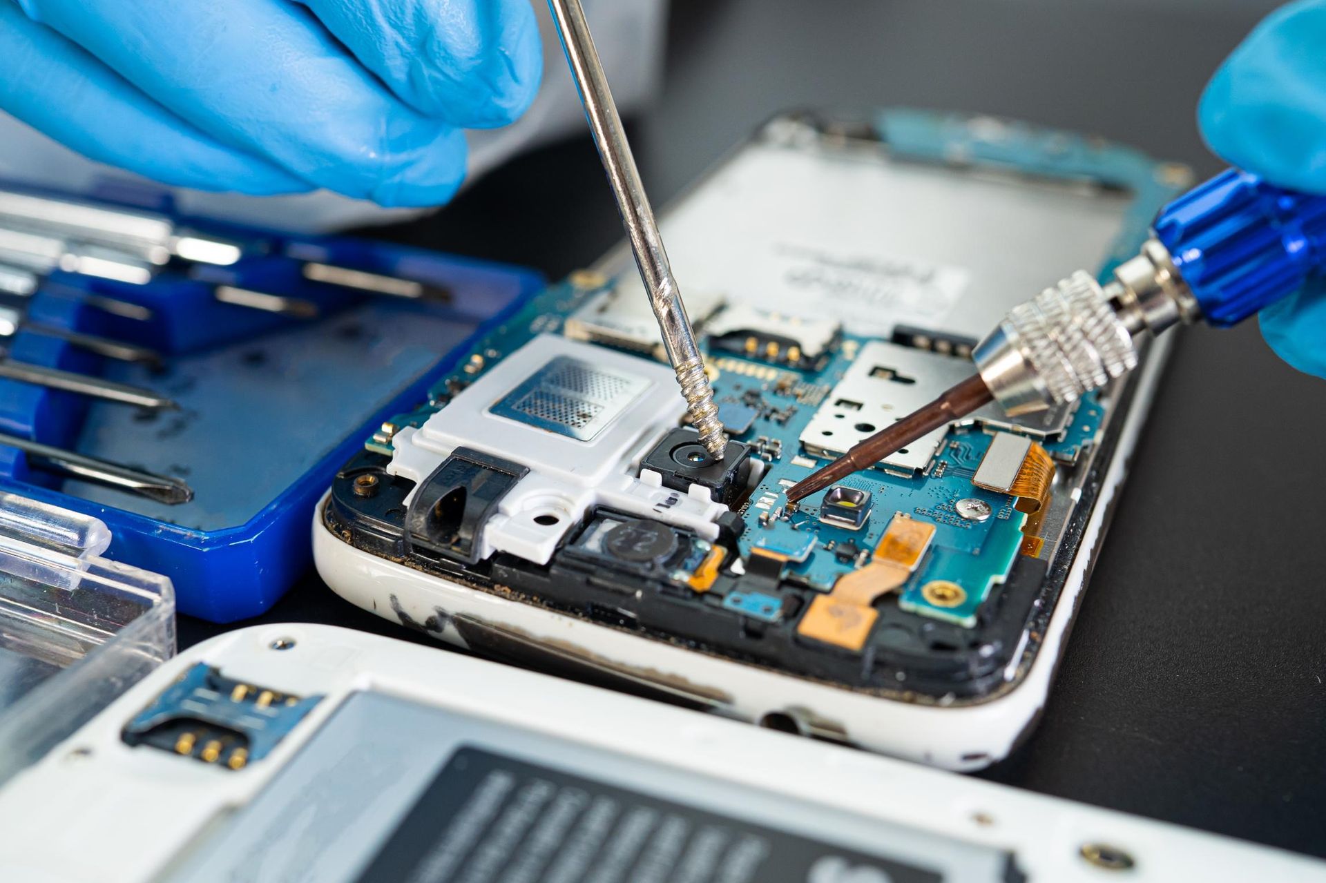 Technician repairing a smartphone motherboard with precision tools on a workbench