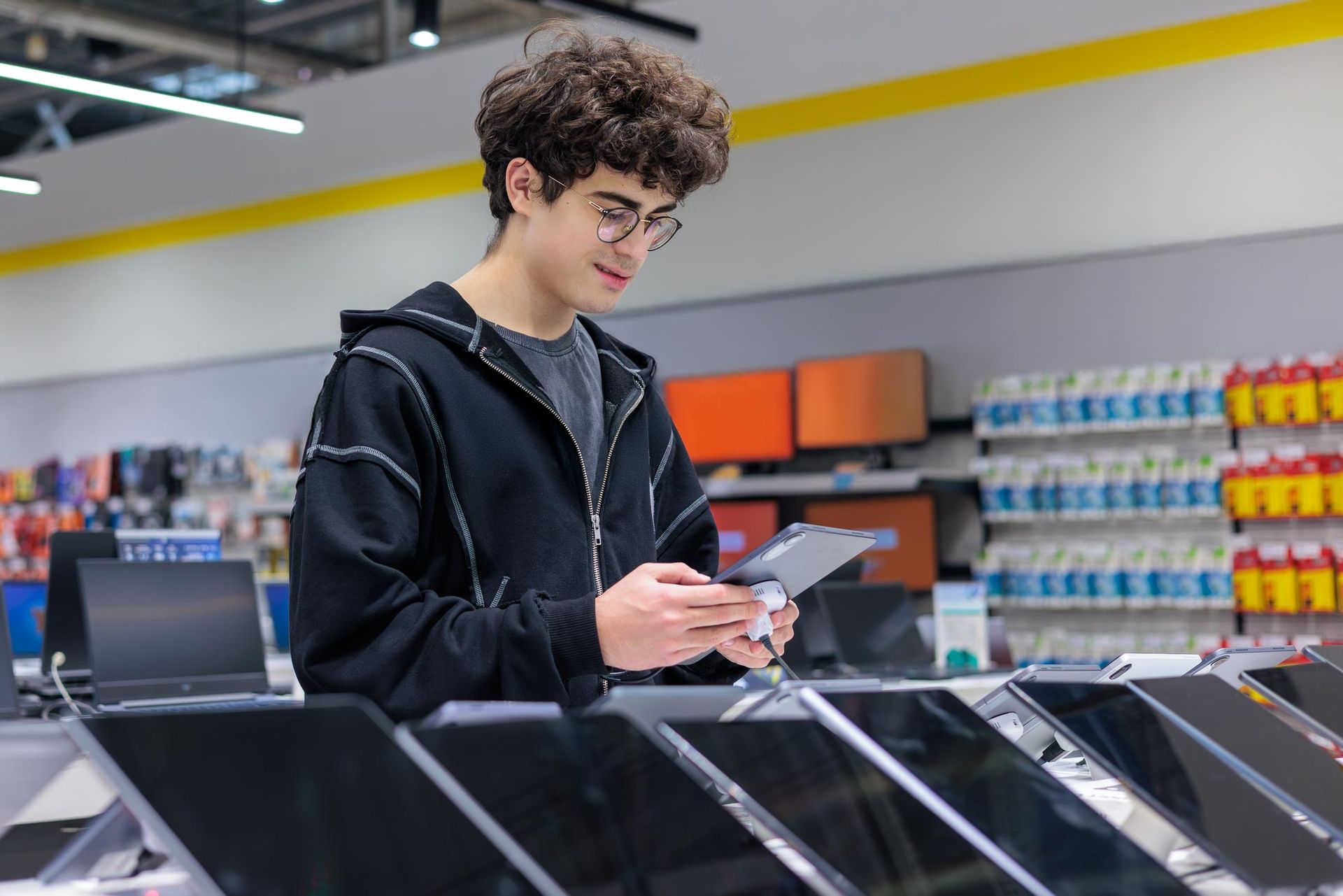 Young man using a smartphone in a retail electronics store near display counters and shelves