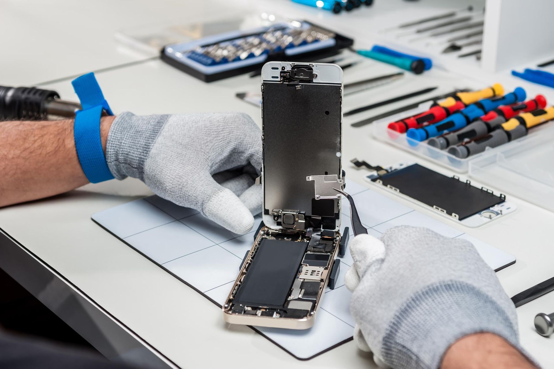 Gloved hands repairing an open smartphone on a workbench with tools and parts nearby