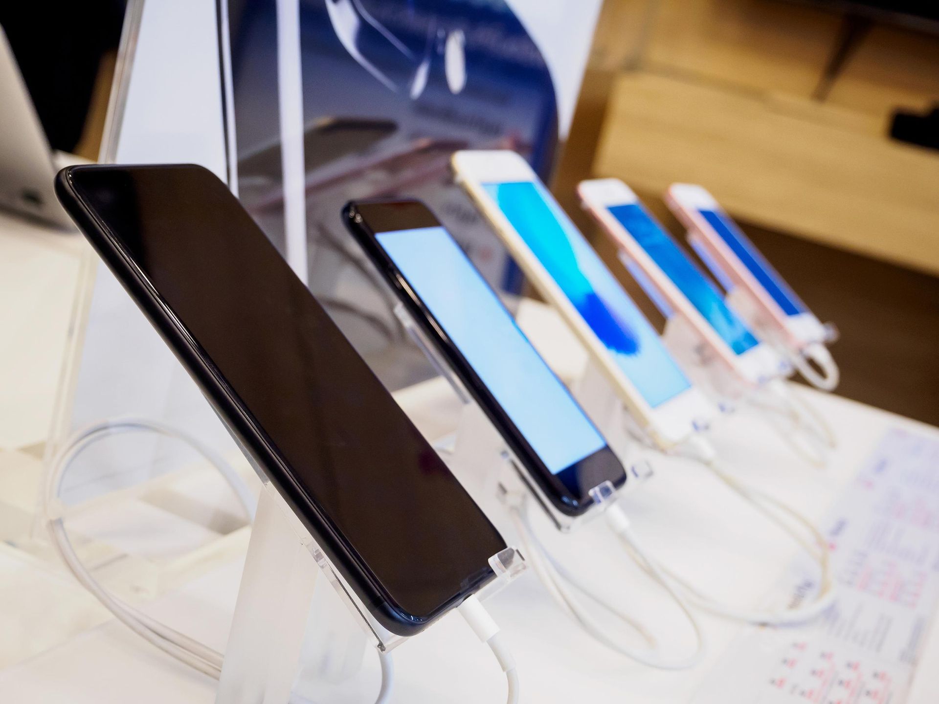 Smartphones displayed on clear stands at a retail counter, showing black, silver, and blue screens