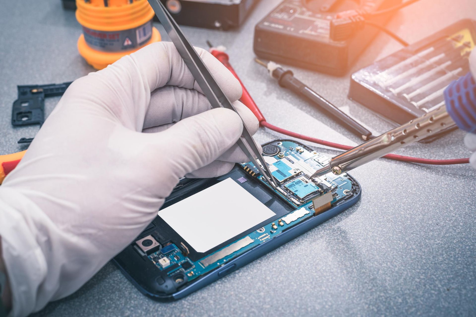 Gloved hands repairing a smartphone circuit board with precision tools on a workbench