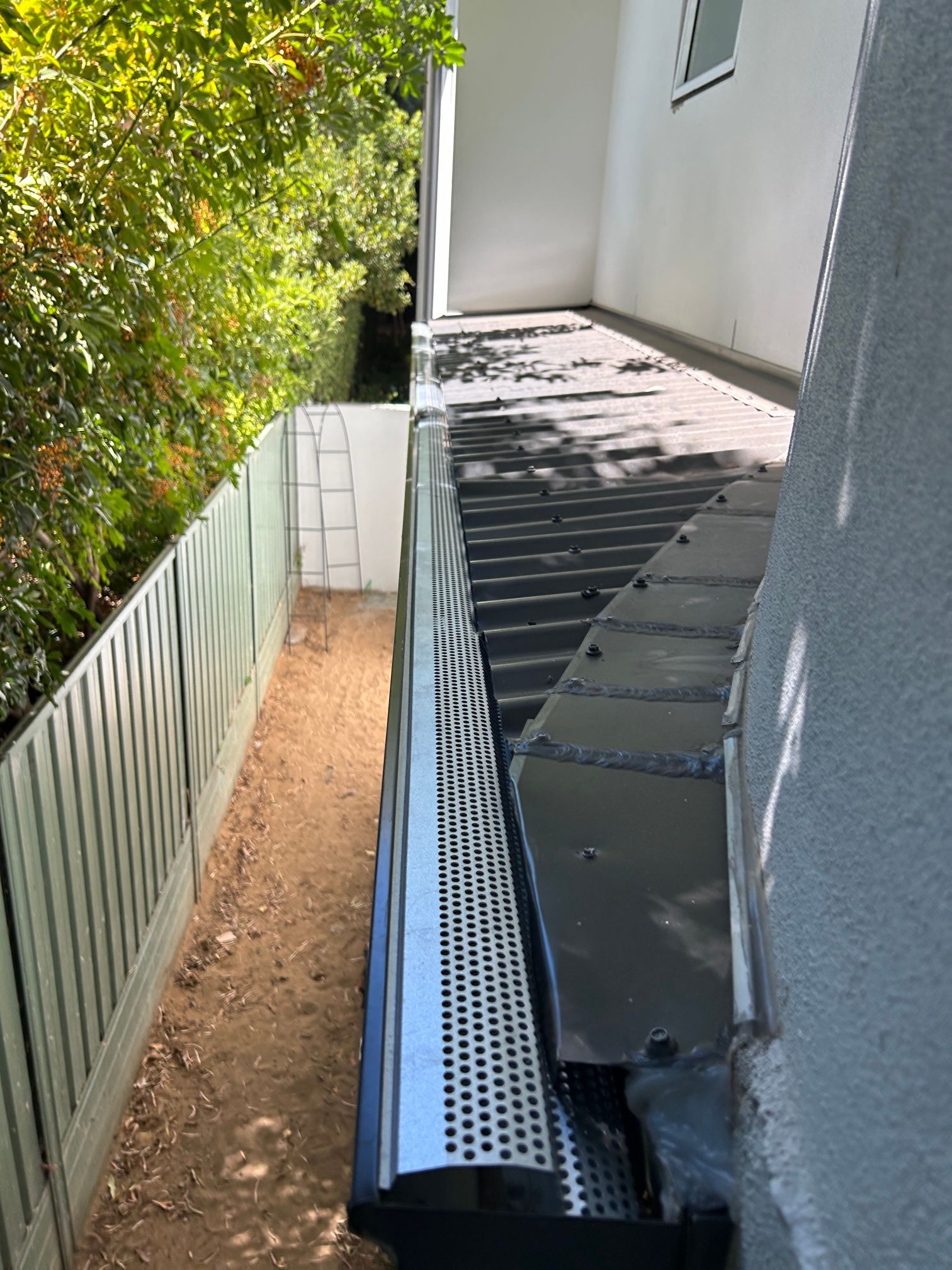 A gutter on the side of a house next to a fence.