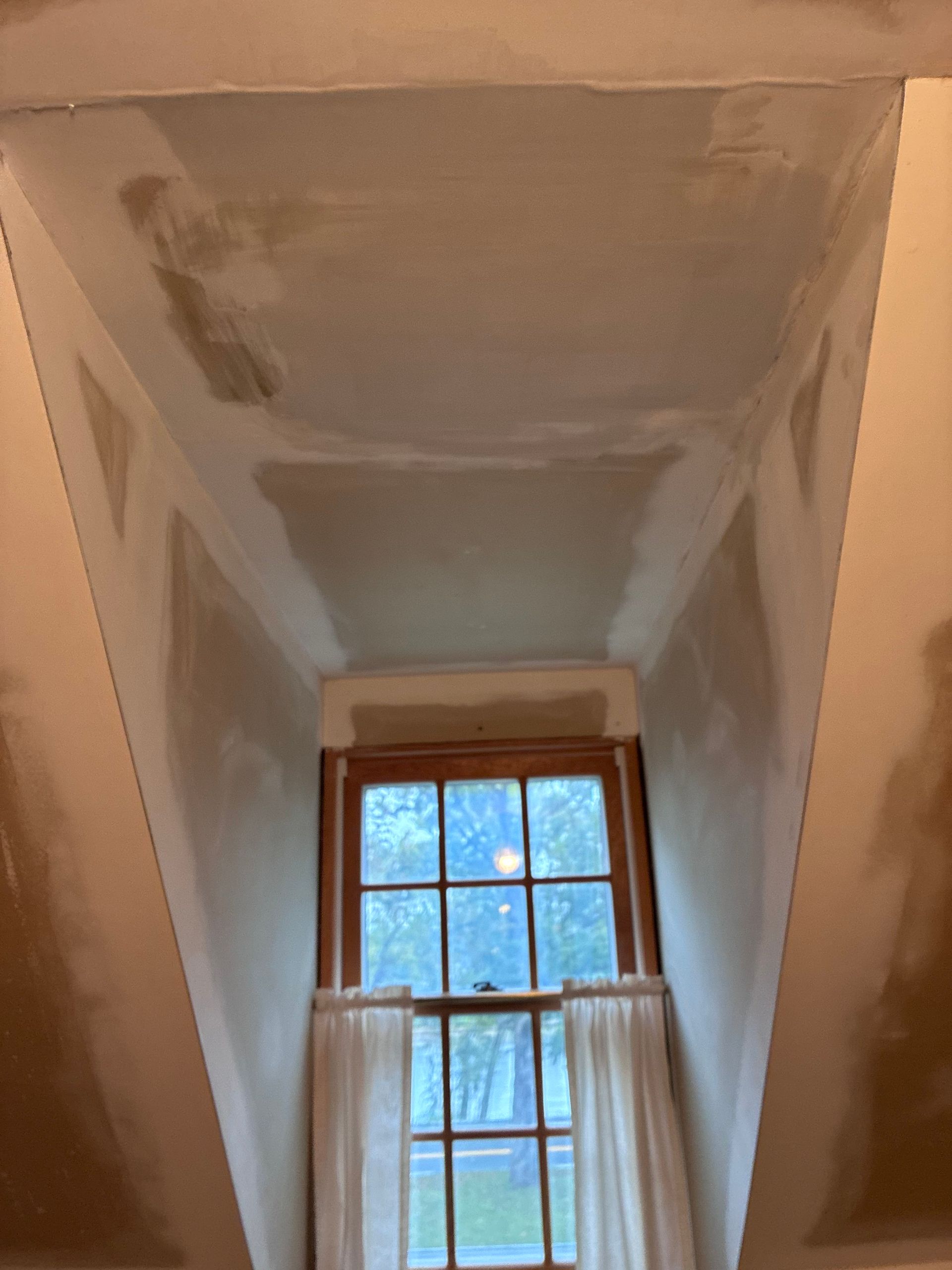 Interior view of a room with a window, newly plastered ceiling, and unfinished walls.