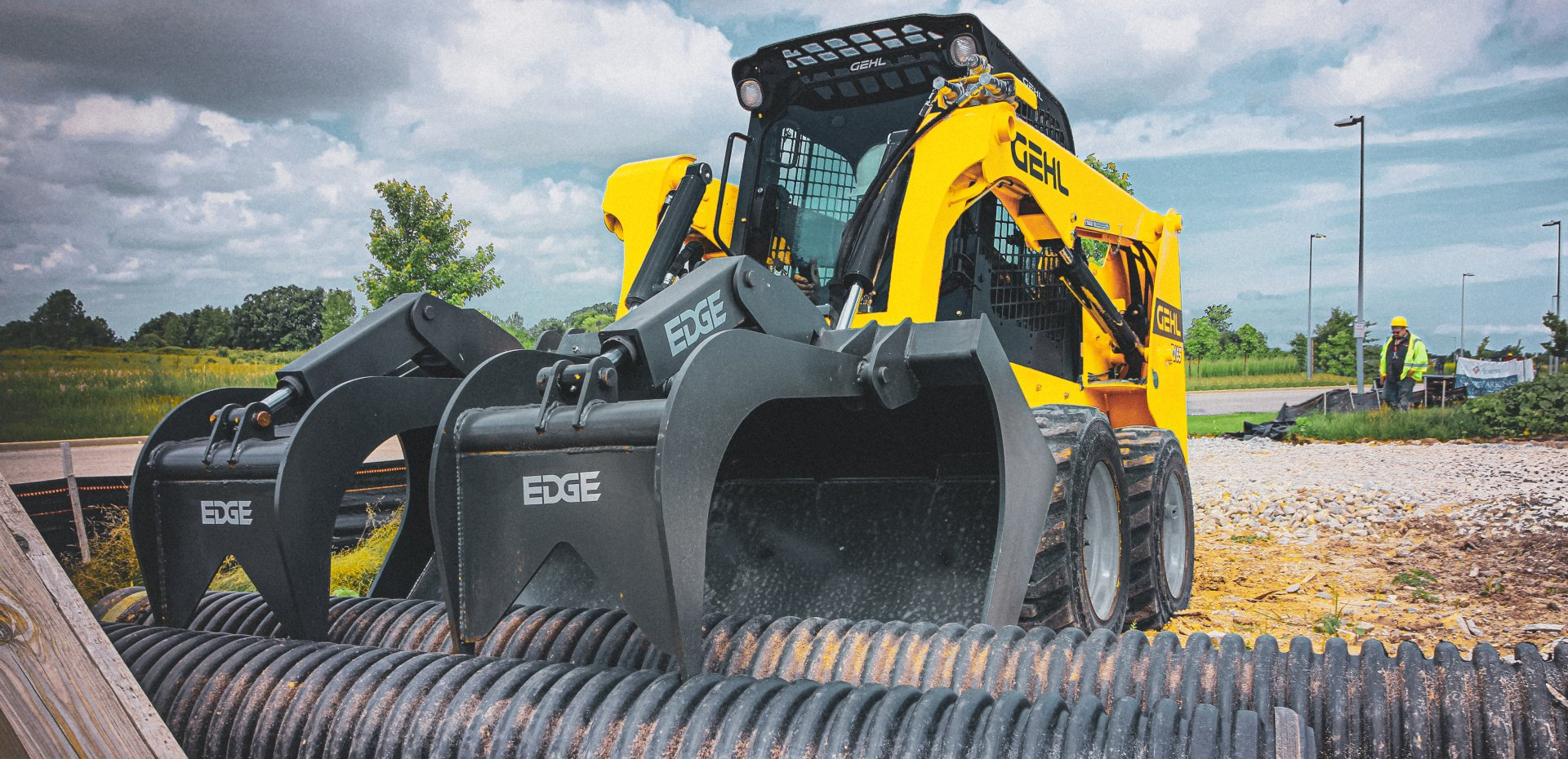 gehl r165 skid steer photo with grapple picking up drain pipes