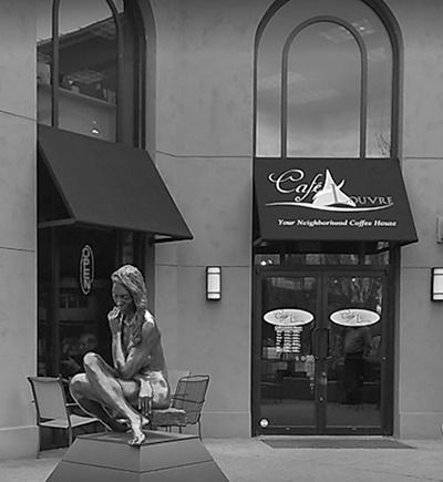 A black and white photo of a statue in front of a cafe