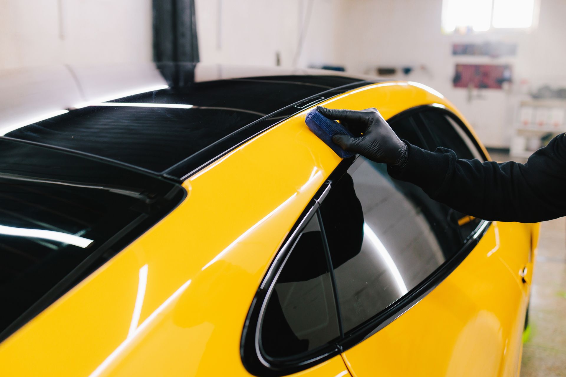 Person in black glove applies ceramic coating to a bright yellow car's roof.