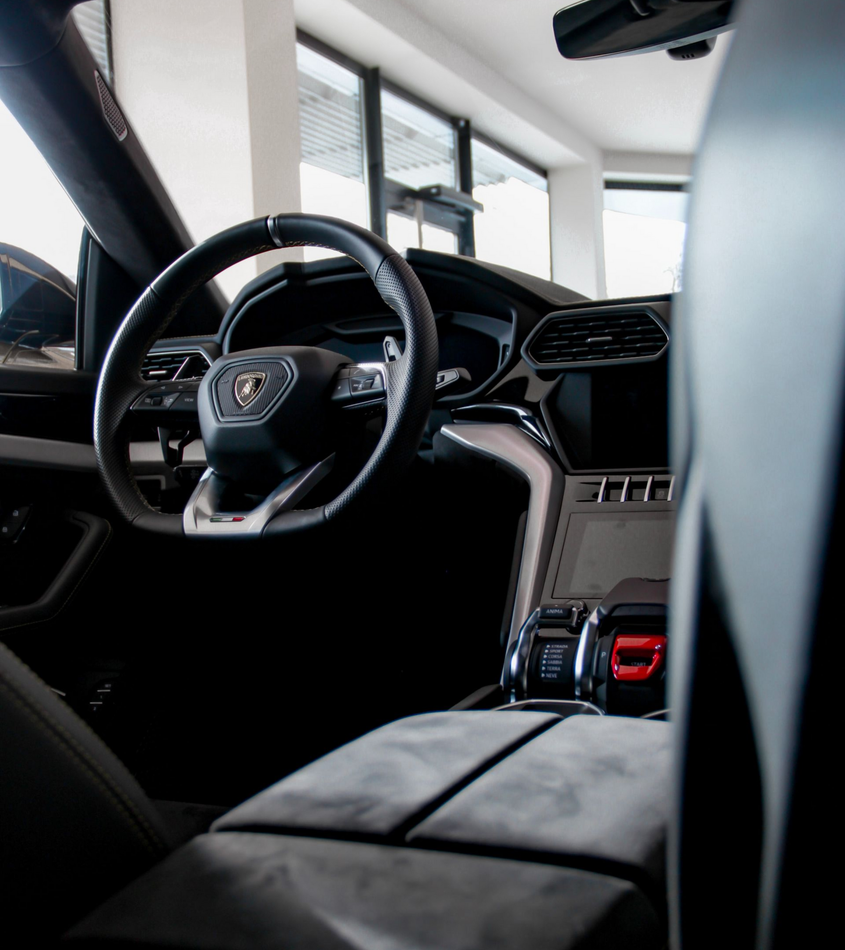 Interior of a black Lamborghini Urus SUV, steering wheel visible.