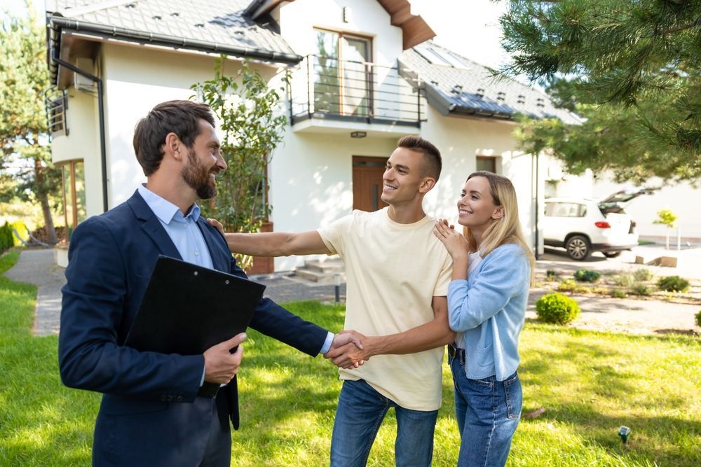 A real estate agent shaking hands with a couple outside a suburban house on a sunny day.