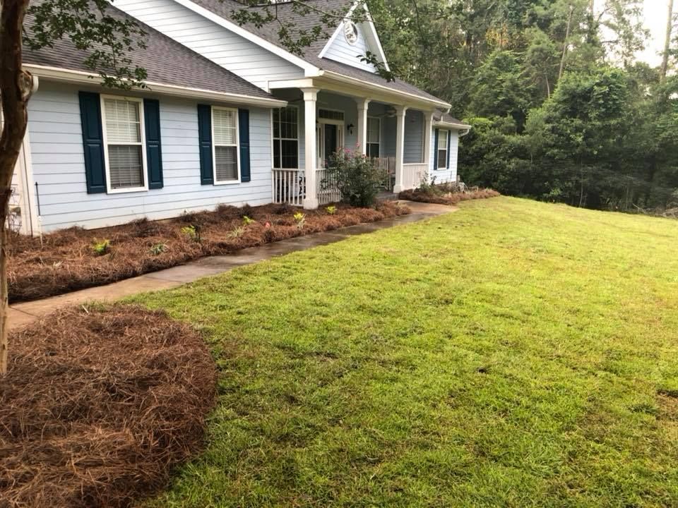 Front yard with fresh mulch beds and a white house with black shutters and a covered porch.