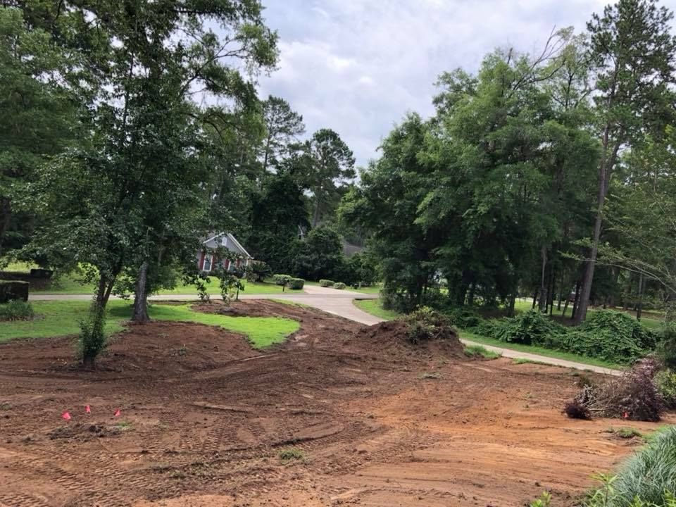 Cleared dirt area beside a winding path in a green, wooded park under cloudy skies