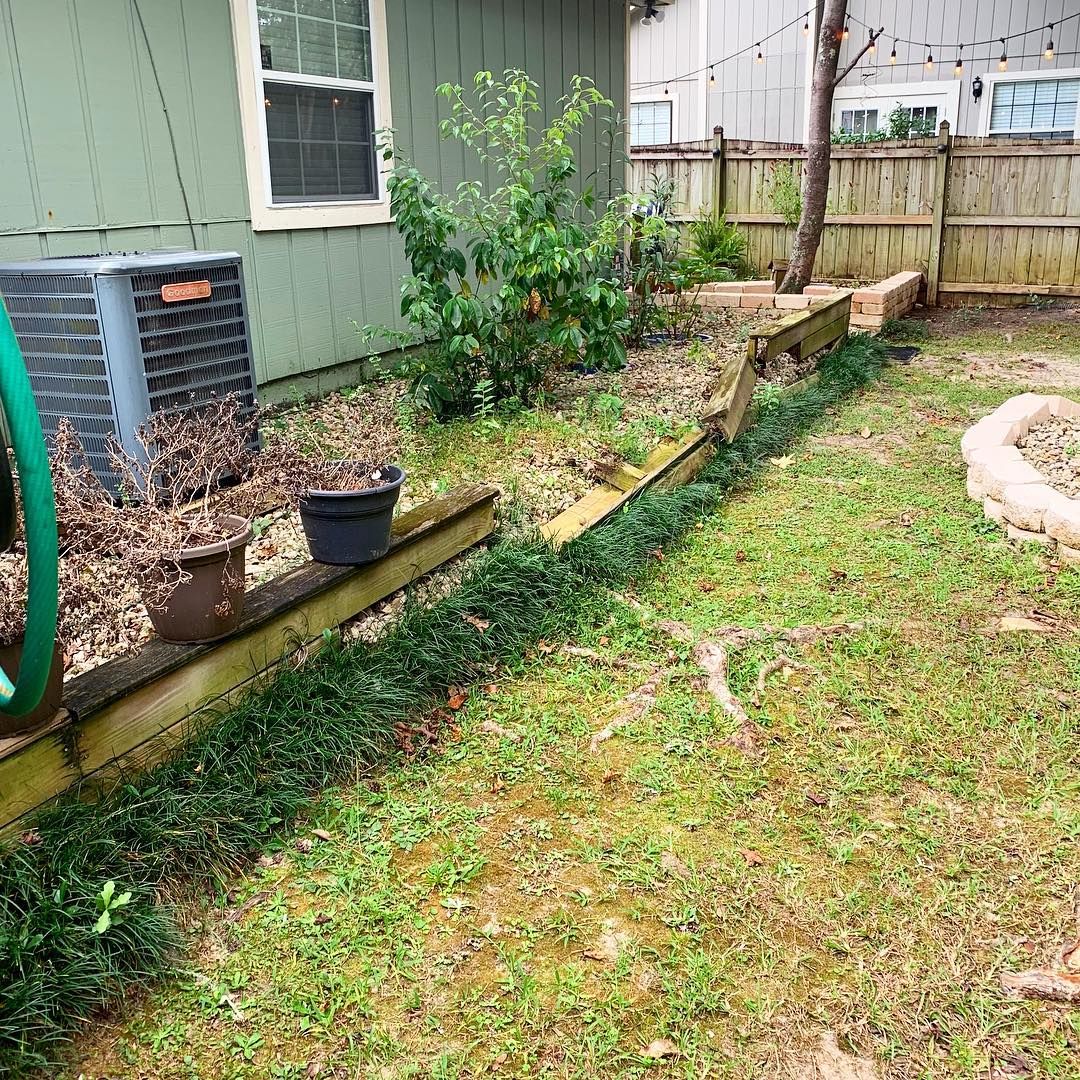 Backyard beside a house with a sloped grassy yard, garden bed, shrubs, and a wooden fence