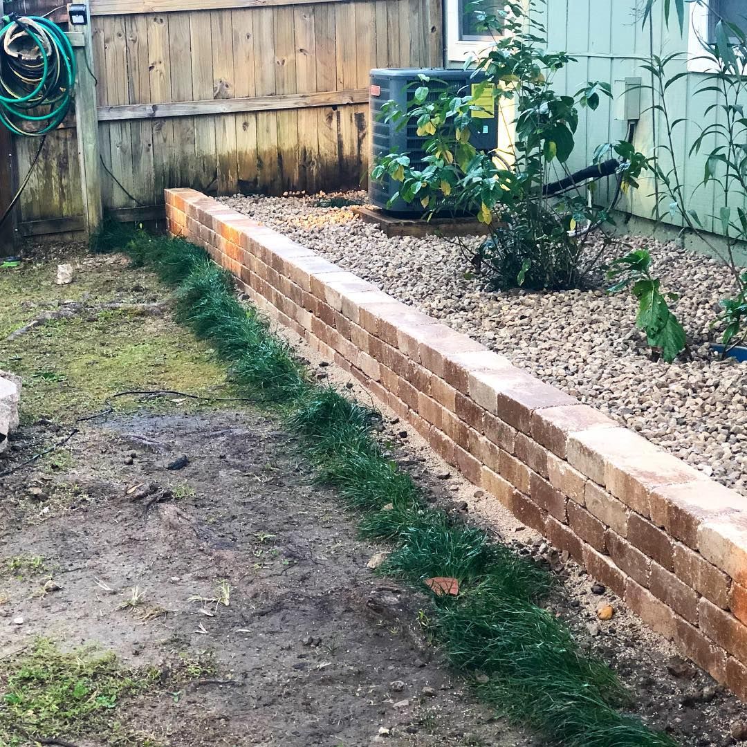 Backyard with a low brick retaining wall beside a wooden fence and garden beds.