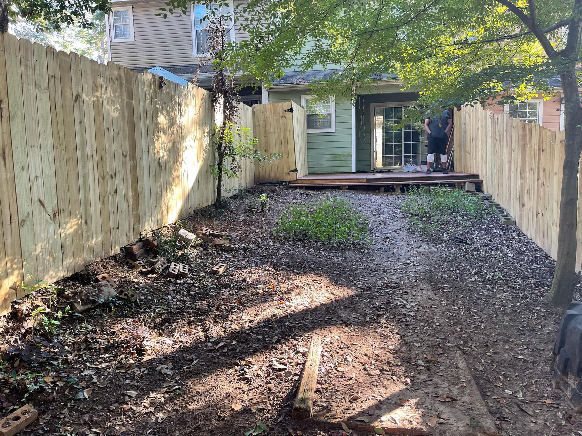 Narrow gravel backyard path between wooden fences leading to a house patio with sliding doors.