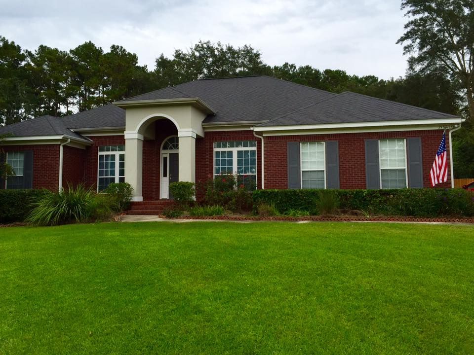 Single-story red brick house with white columns, green lawn, and an American flag.