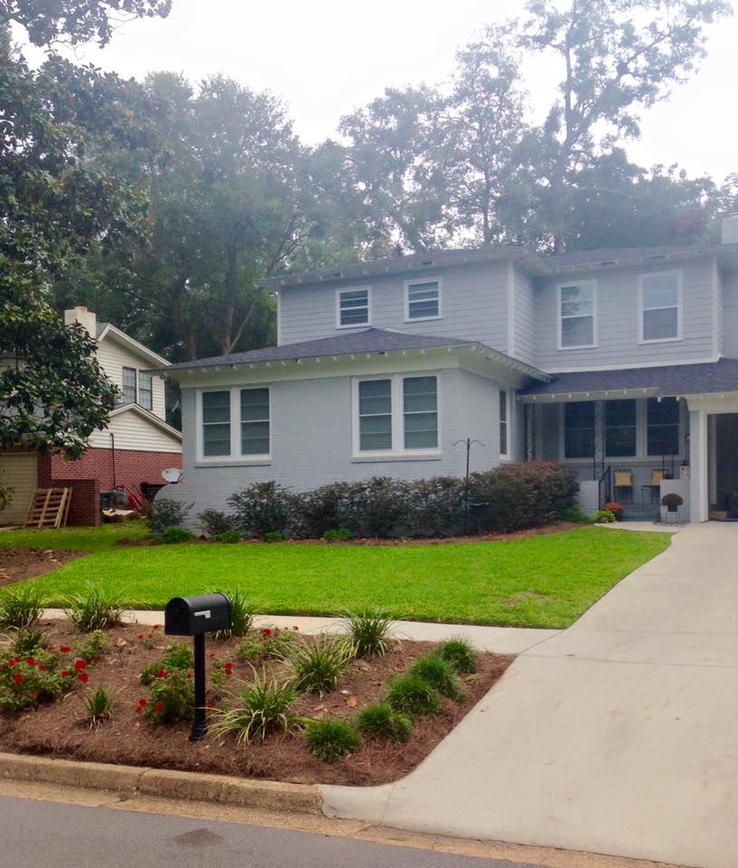 Suburban two-story gray house with white trim, front lawn, flower bed, and driveway