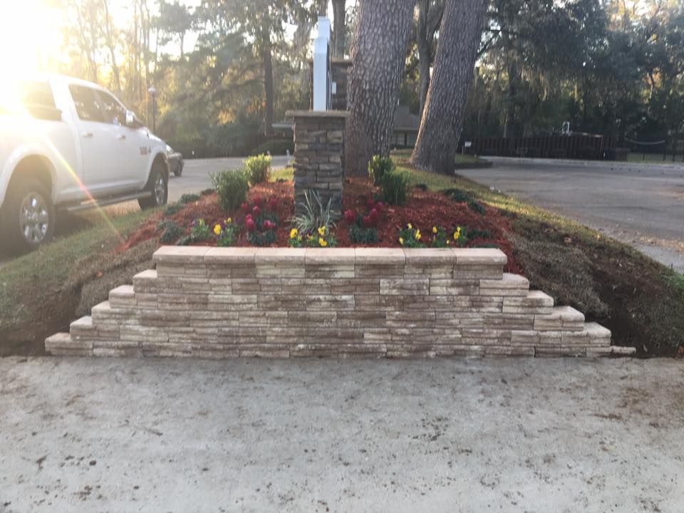 Landscaped brick flowerbed with red blooms and stone steps in front of a yard signpost