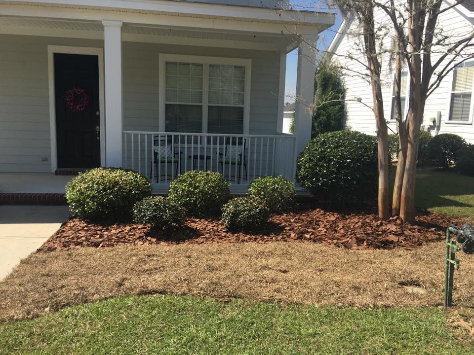 Single-story house porch with white railings, shrubs, and a bare front lawn.
