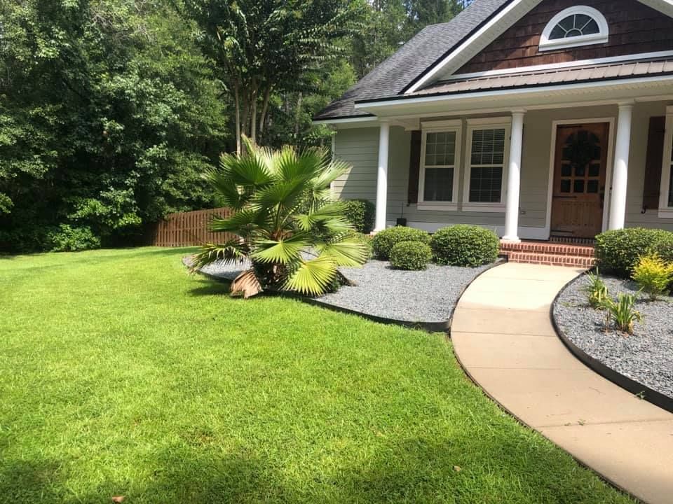 Front lawn with landscaped garden, curved walkway, and house entrance with white trim and dark roof.