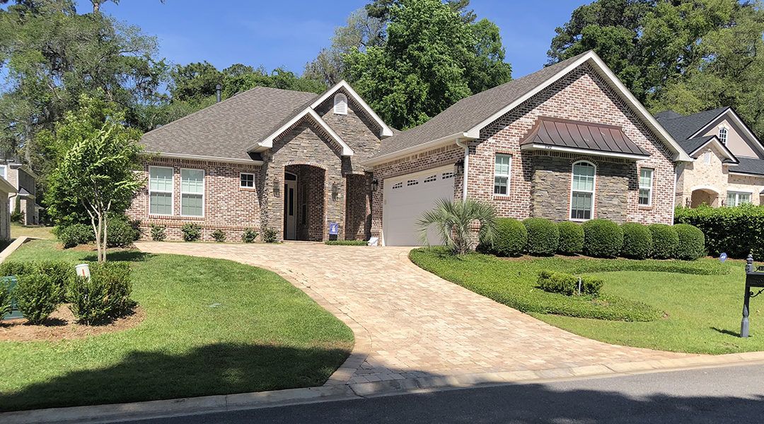 Suburban brick house with stone entry, sloped driveway, and manicured lawn on a sunny day