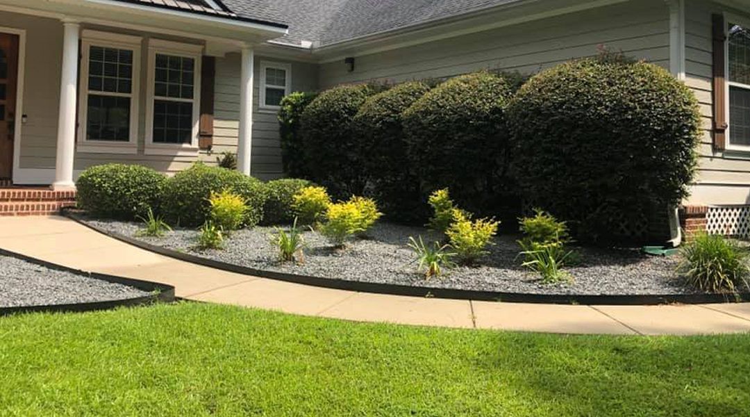 Landscaped front yard with trimmed shrubs, flower beds, and a house entrance