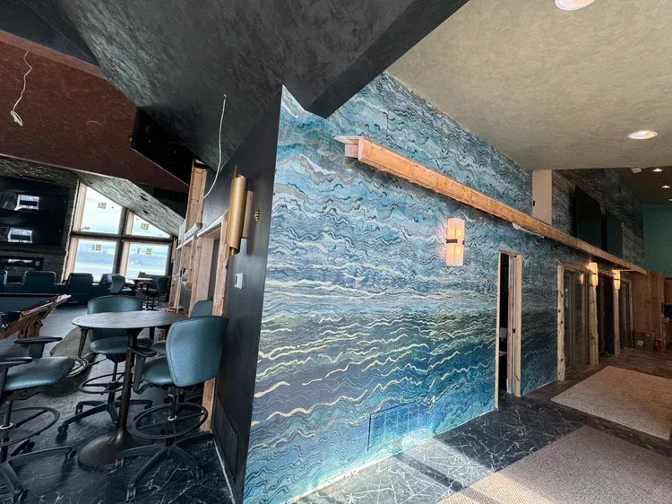 A lounge area features a blue, wave-patterned feature wall, a dining table with chairs, and warm ambient lighting.