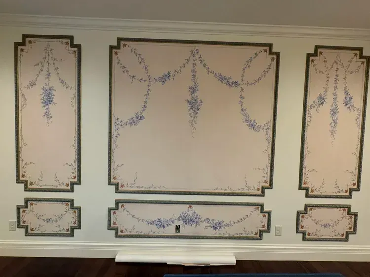 A pale pink wall with decorative dark trim panels, each hand-painted with blue floral garlands and swags.