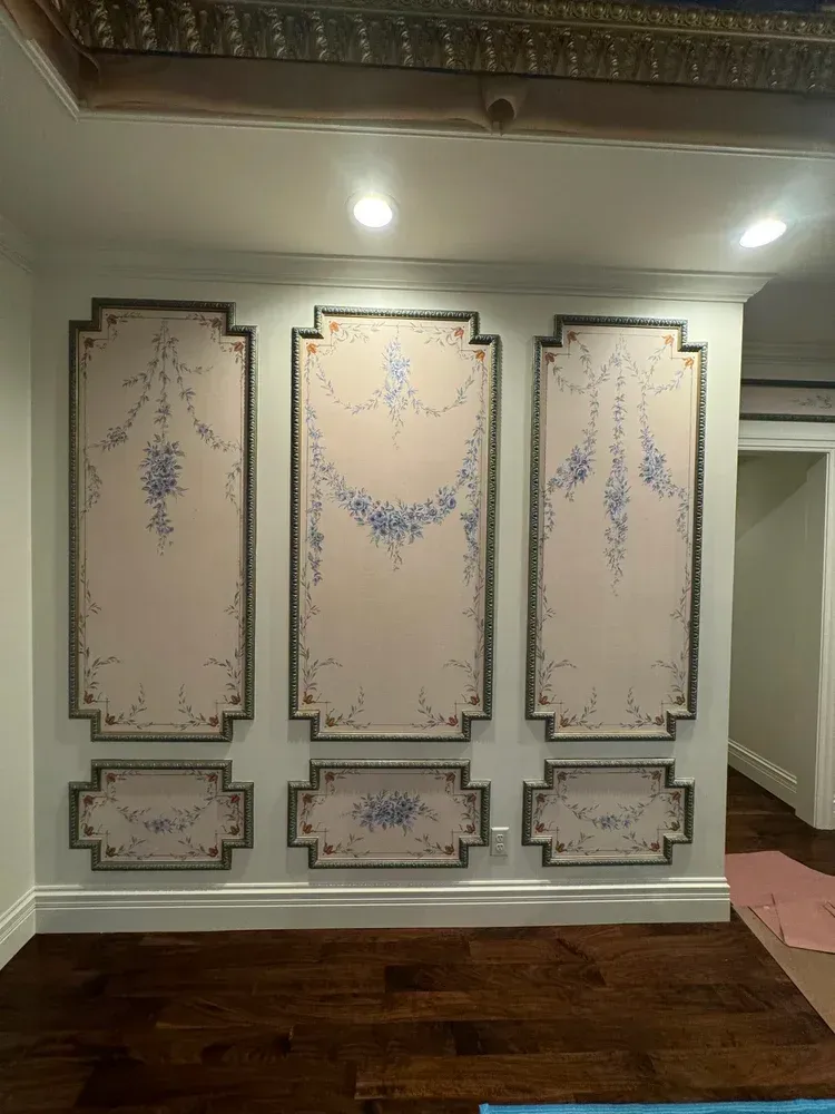 Three rectangular wall panels with painted floral swags in blue on a pale pink background, framed by molding.