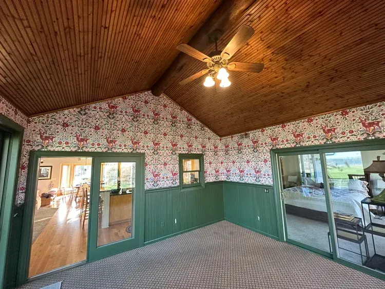 A room with wood-paneled vaulted ceilings, deer-patterned wallpaper, green wainscoting, and sliding glass doors.