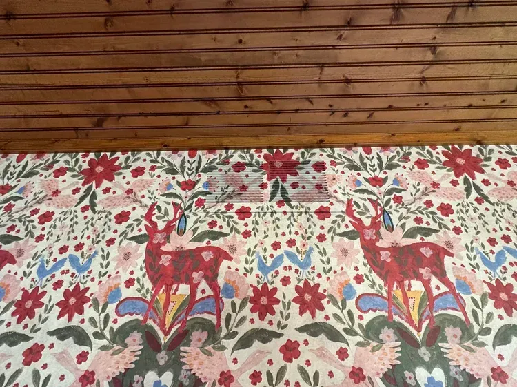 Wallpaper with a repeating folk-art pattern featuring red deer, white flowers, and blue accents, below wood paneling.