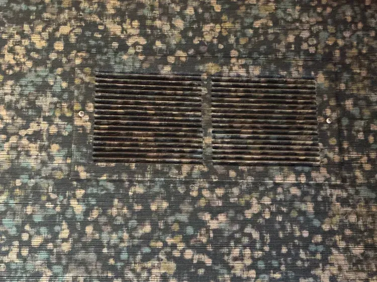 A rectangular metal floor vent centered on a dark, multi-colored speckled patterned carpet.