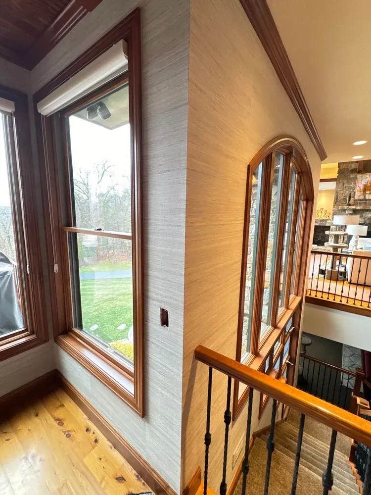 A corner of a room featuring textured light-colored wallpaper, wood trim, a window, and a staircase looking down into a home.