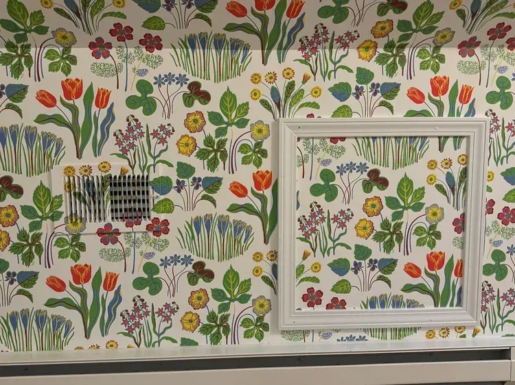 Wall with colorful floral wallpaper featuring tulips, a white rectangular frame, and a vent on the left side.