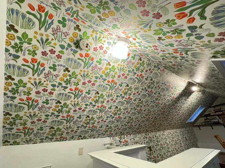 A room featuring sloped walls covered in colorful floral wallpaper, with a light fixture on the ceiling.