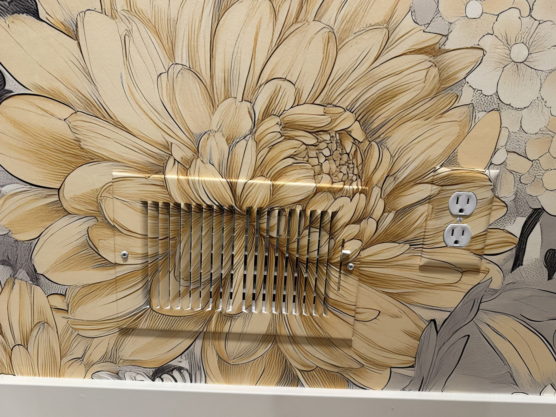A metal air vent and a wall electrical outlet are installed directly onto a wall covered in tan and black floral wallpaper.