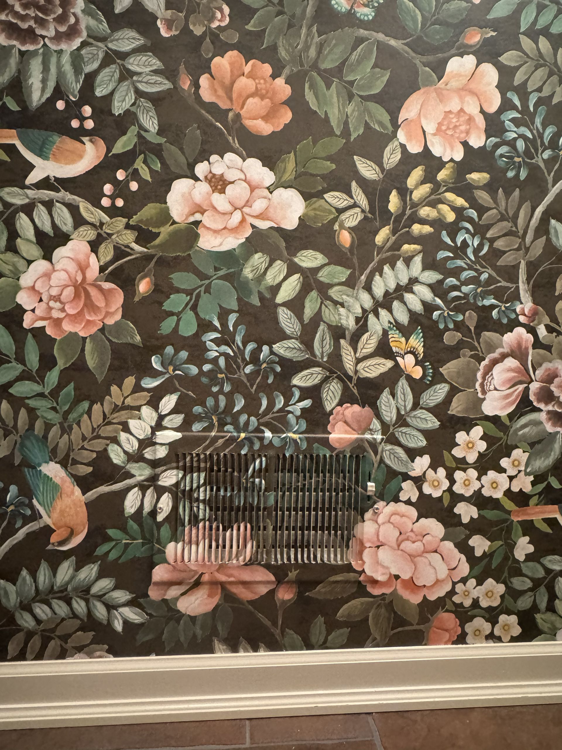 Floral wallpaper with pink flowers, green foliage, and birds on a dark background, featuring a wall air vent in the center.