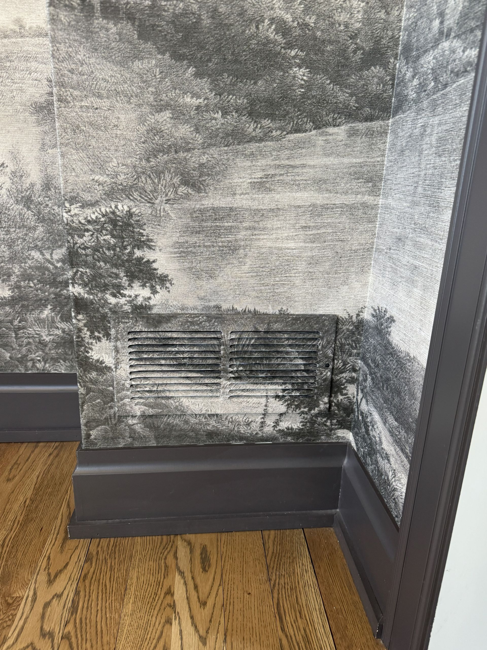 A charcoal-toned mural wall with a horizontal vent, dark baseboards, and hardwood flooring.