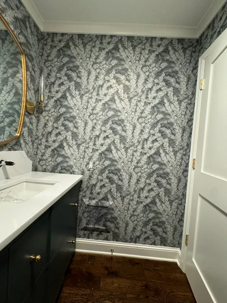 A powder room featuring a dark vanity with a white countertop, gold hardware, and bold gray and white leaf wallpaper.
