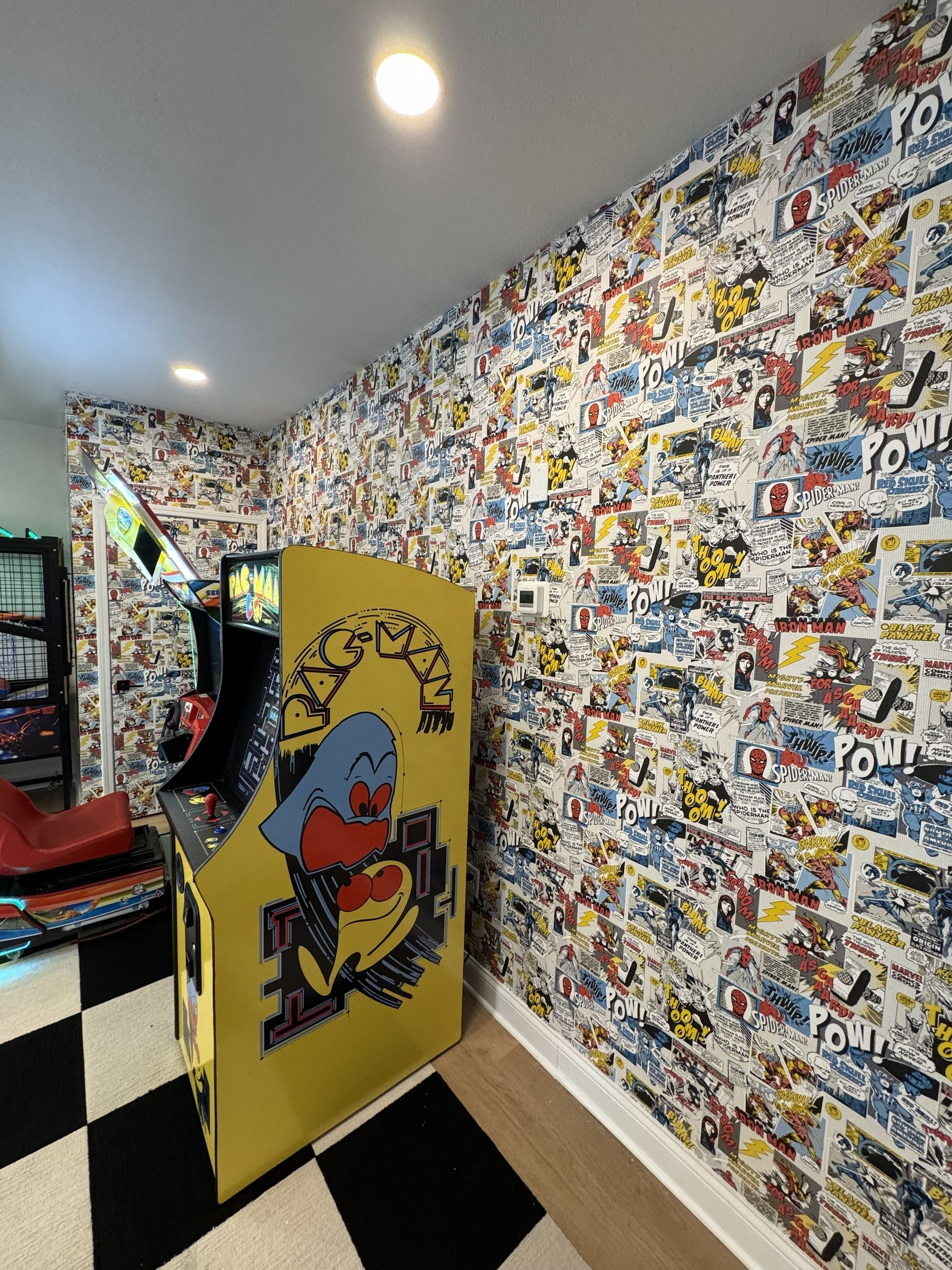 A yellow Pac-Man arcade cabinet stands on a black-and-white checkered floor against a comic-book-patterned wallpaper.