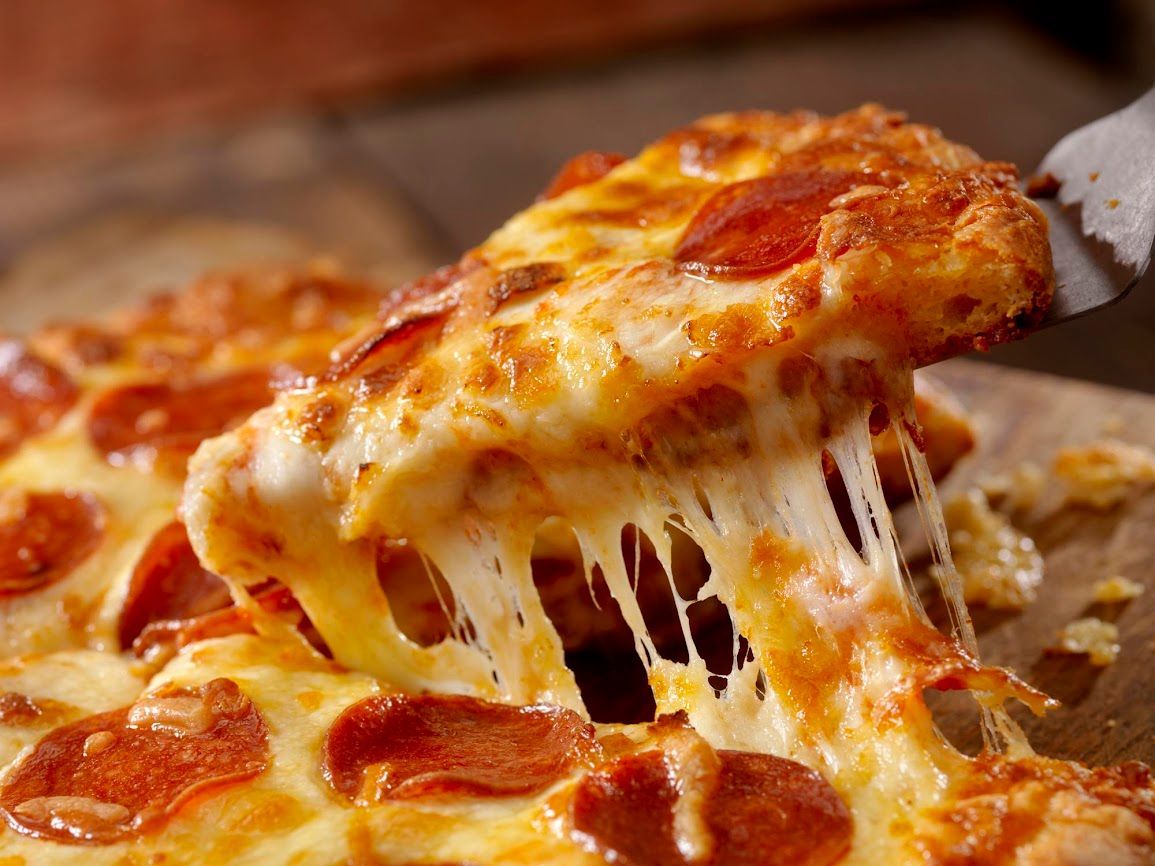 Una fetta di pizza al salame piccante viene sollevata, con il formaggio fuso che fuoriesce dalla pizza