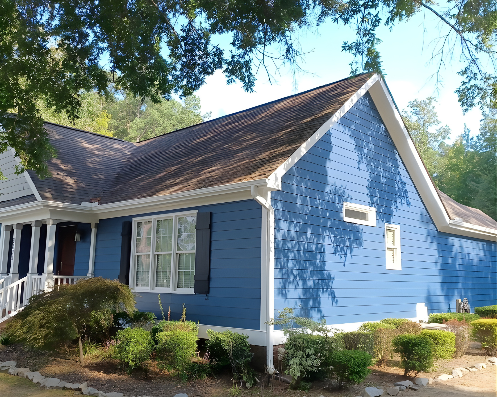 A blue house with white trim, a gabled roof, and black shutters, partially obscured by trees and bushes.