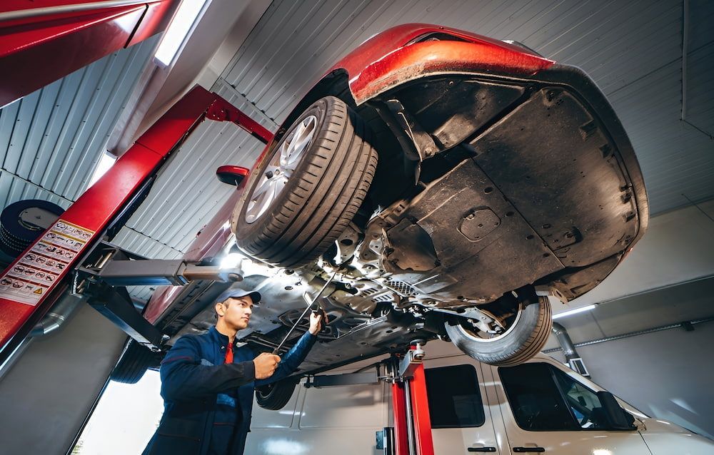 A Man Is Working On A Car On A Lift In A Garage — SJM Autocare in Mullumbimby, NSW