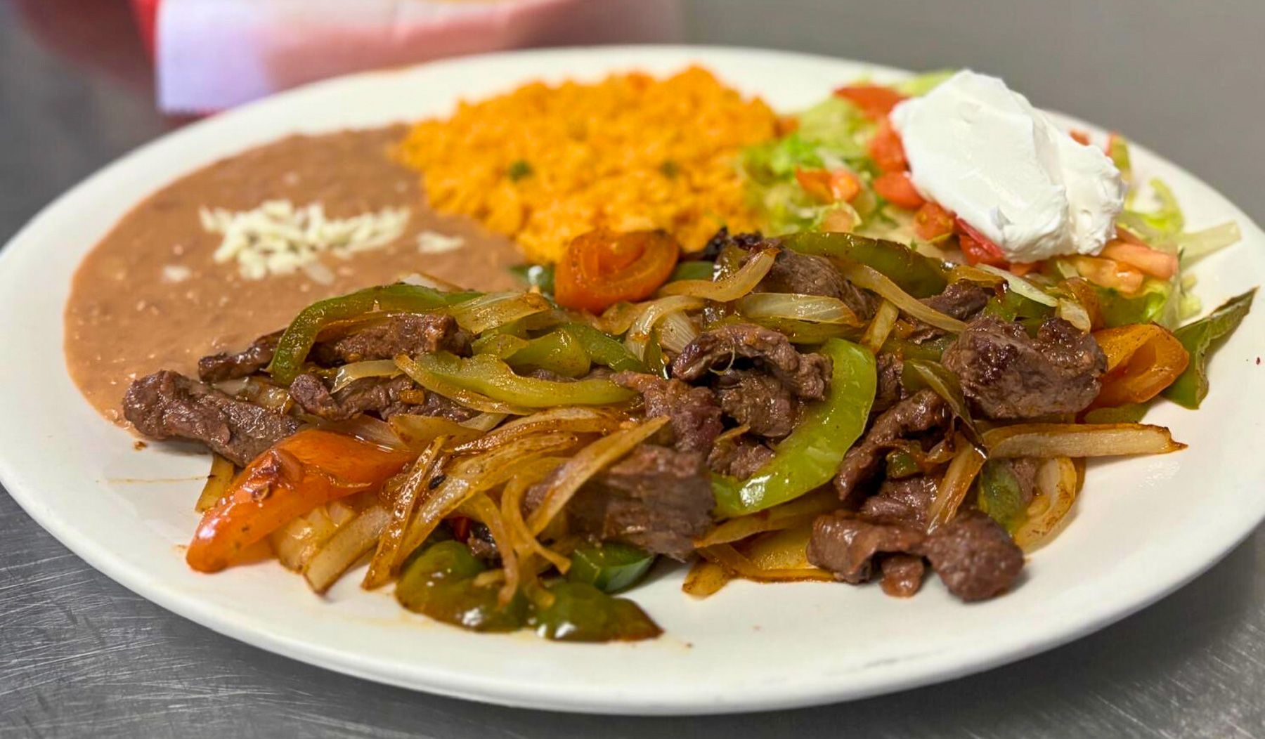 Steak fajitas sizzling with peppers, onions, rice, and beans