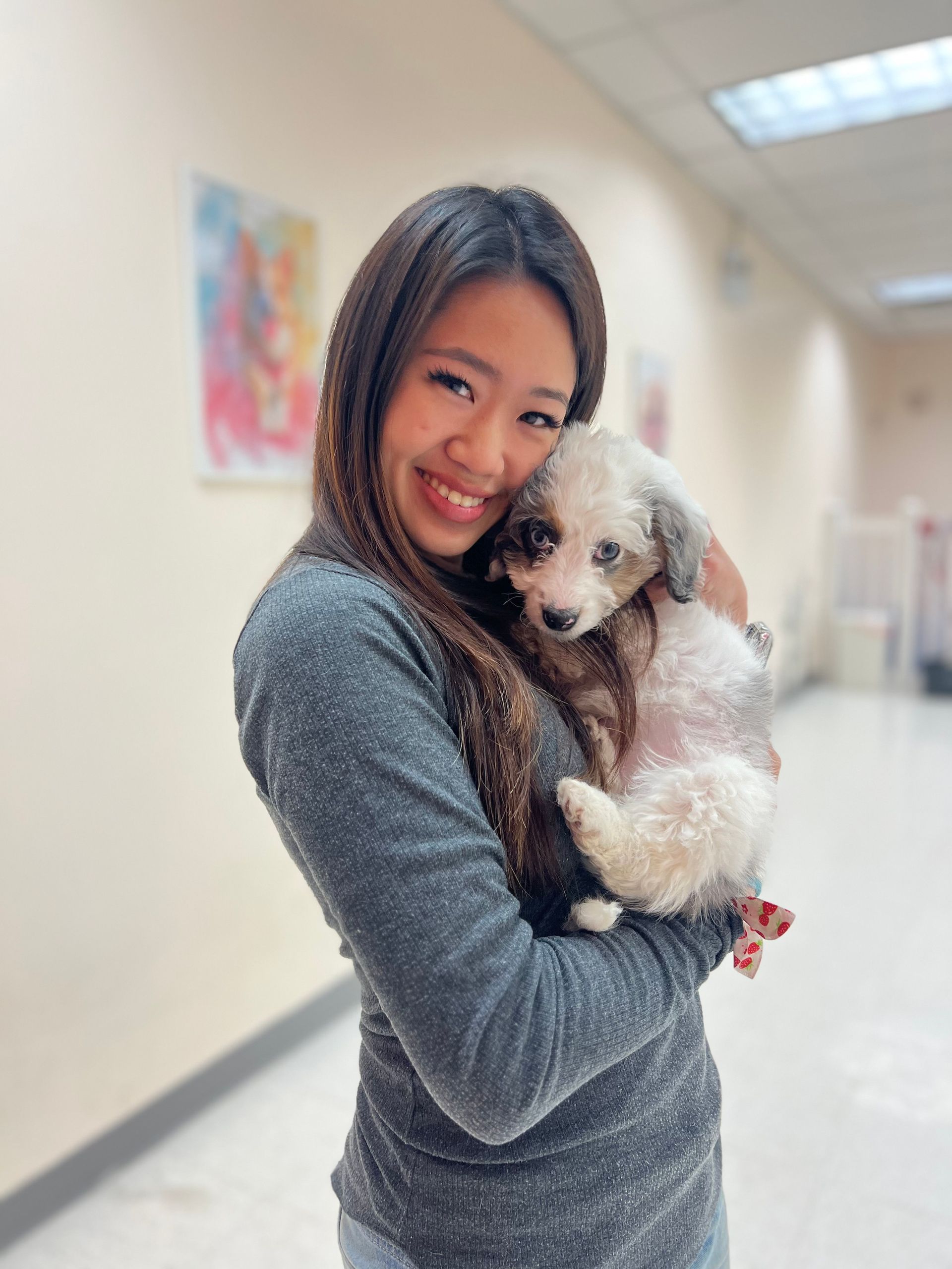 Woman smiling and holding a small fluffy dog in a hallway, with a blurred colorful wall art background