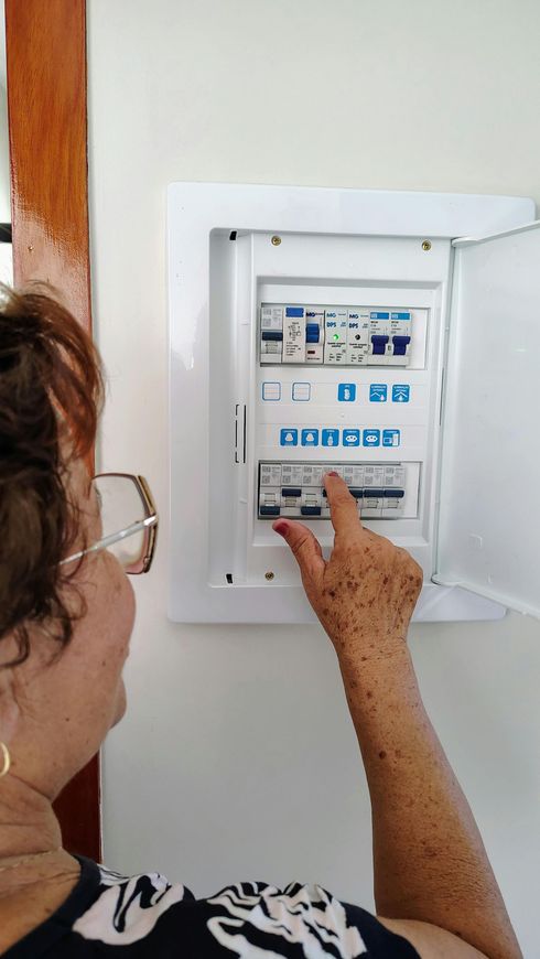 Un elettricista, con indosso un elmetto, occhiali di sicurezza e un giubbotto ad alta visibilità, utilizza un multimetro per testare un interruttore automatico.