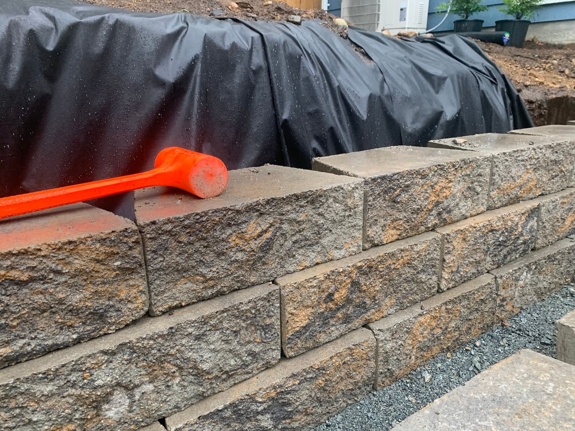 Red-handled trowel resting on a stone retaining wall beside a covered object outdoors