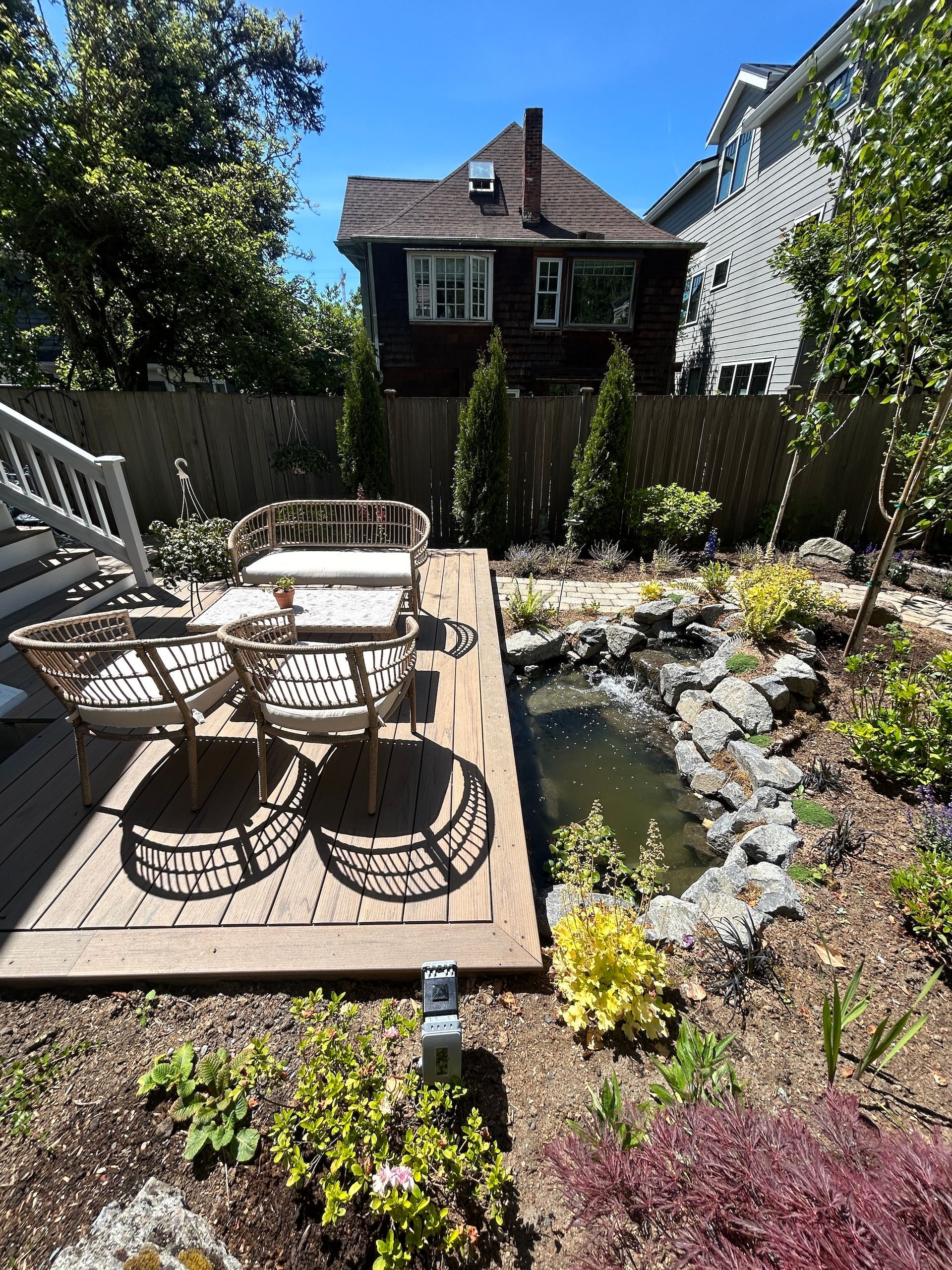 Backyard patio with wicker chairs, wooden deck, and a small pond beside a garden shed