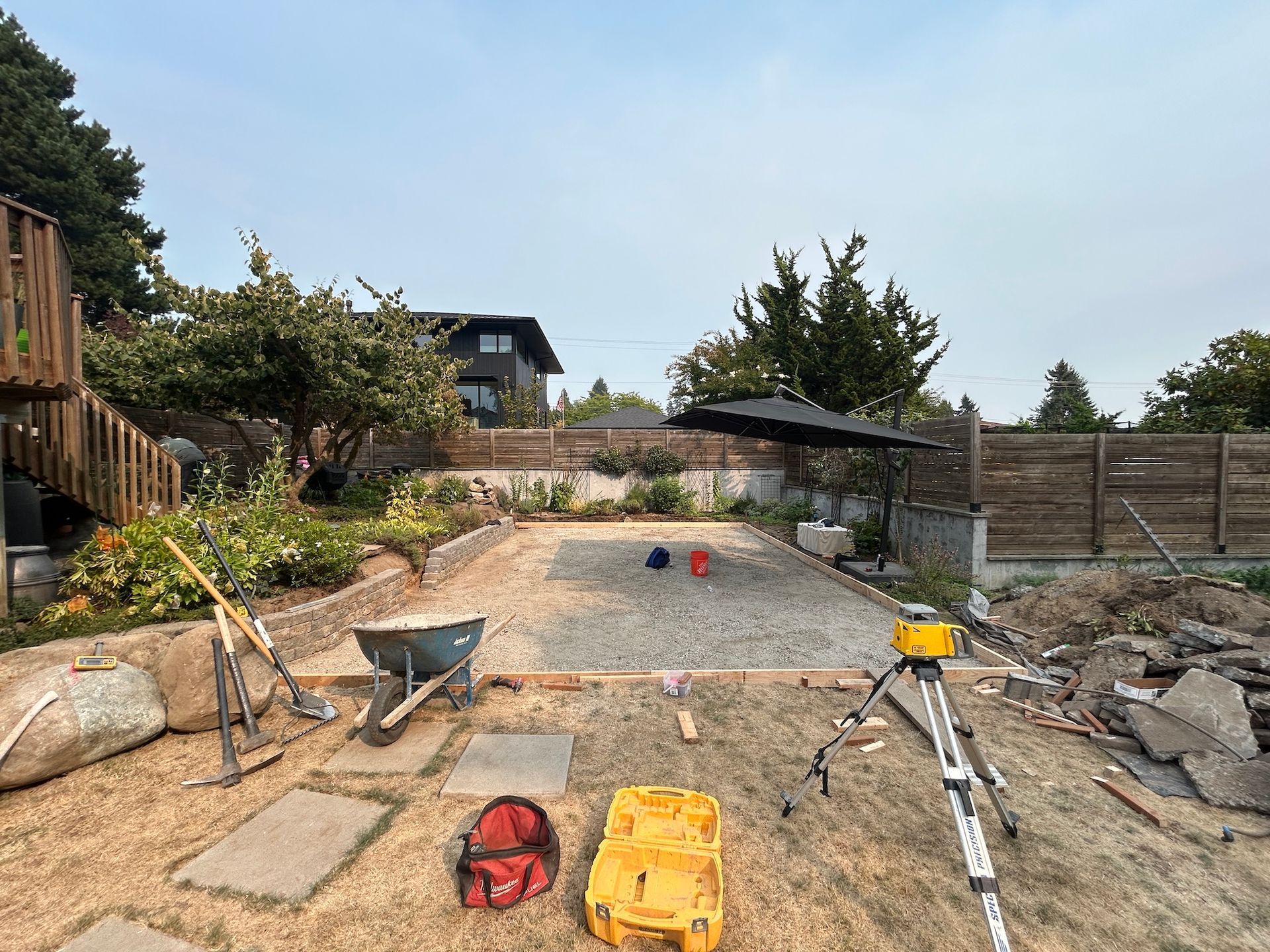 Backyard gravel worksite with tools, wheelbarrow, and fence under construction